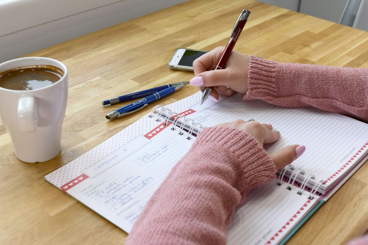 A person writing in a notebook with coffee