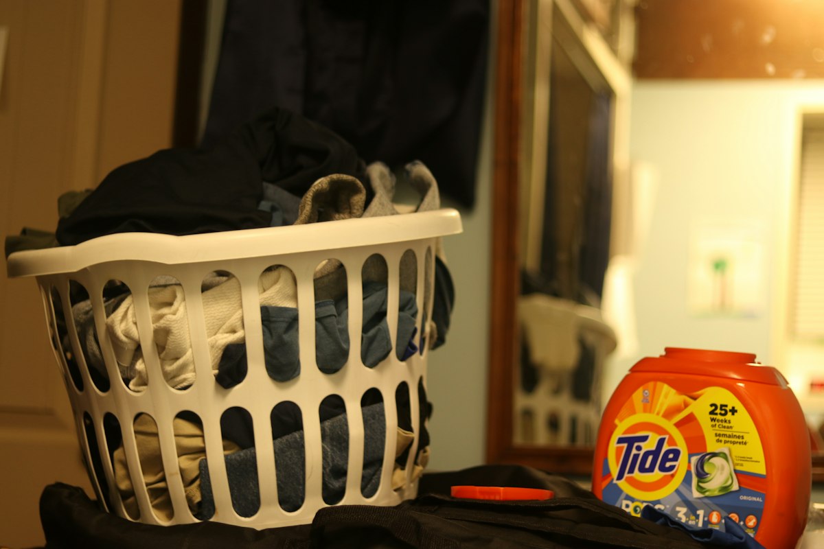 a laundry basket filled with clothes next to a bottle of tide