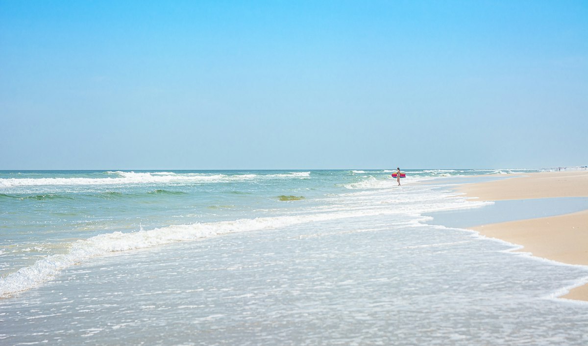 A person walks along a sandy beach with gentle waves