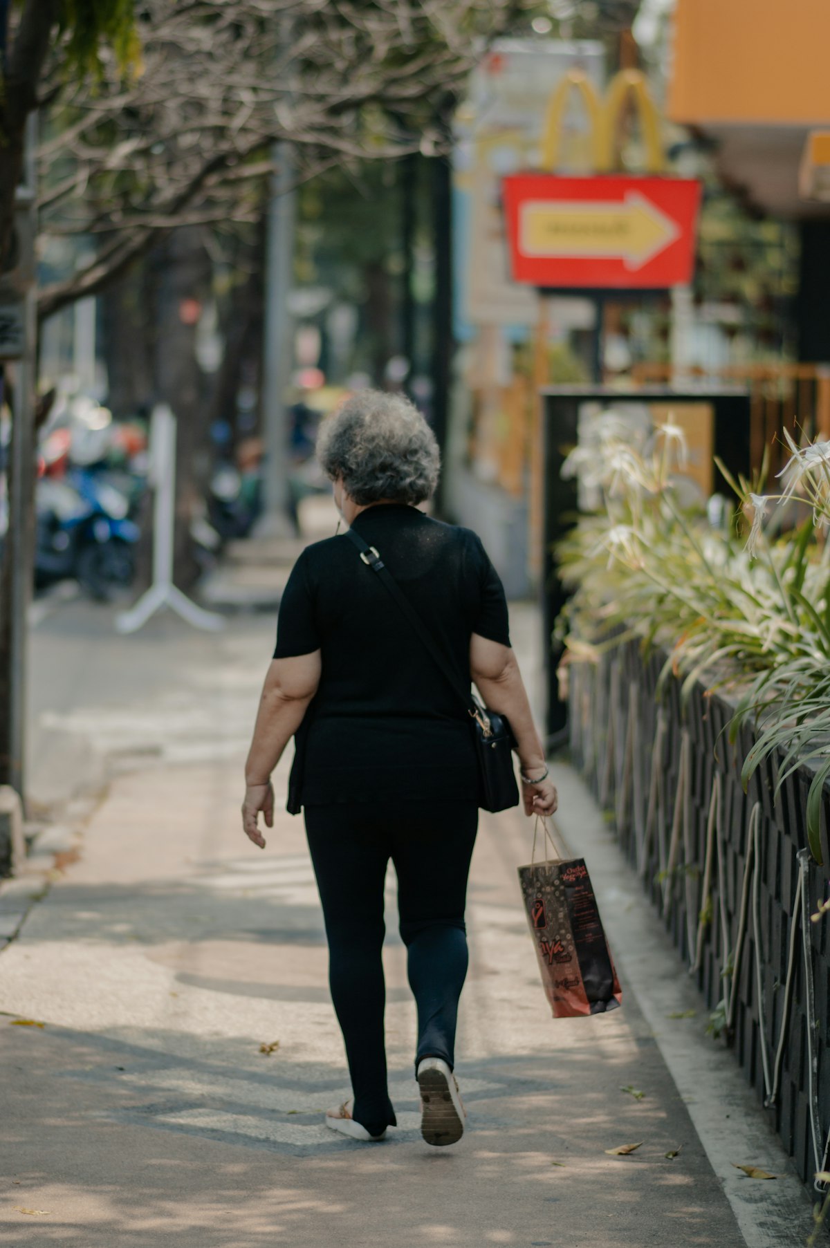 a woman walking down a sidewalk carrying a shopping bag