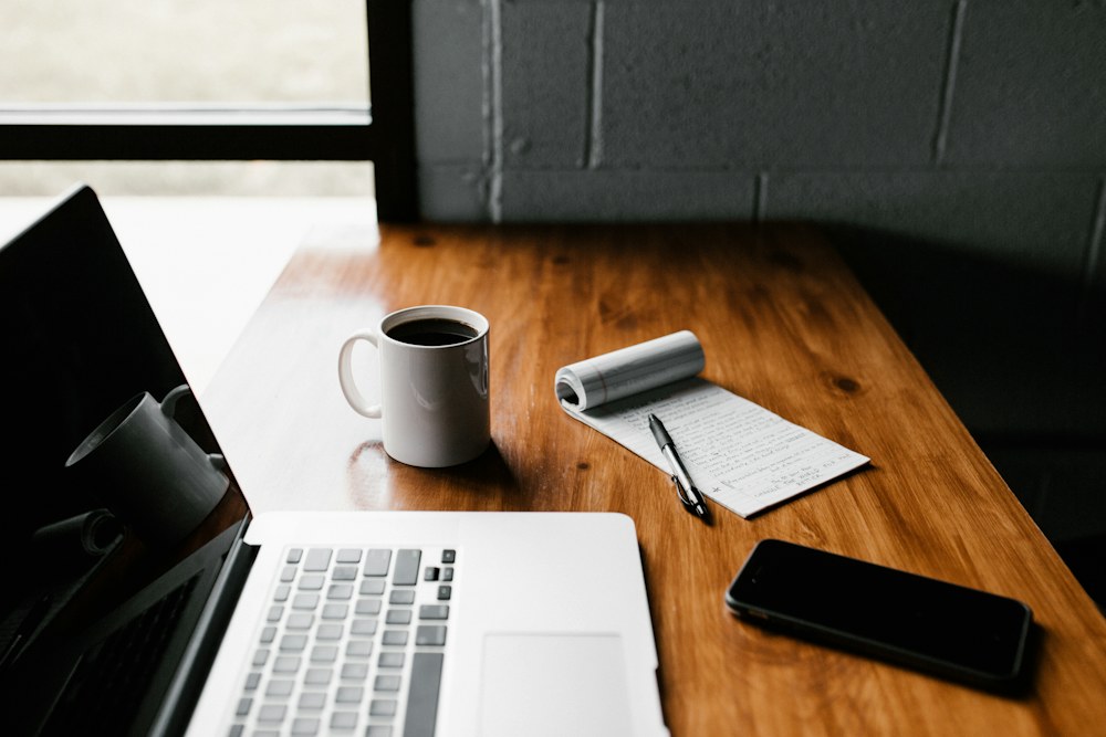 Notebook, laptop, and coffee on a work table